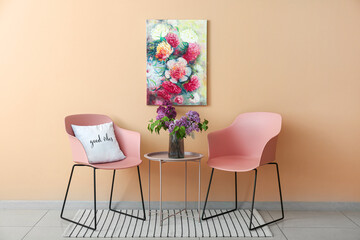 Modern pink chairs and glass vase with lilac flowers on table near color wall