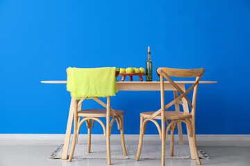 Dining table with apples and bottle of wine near color wall
