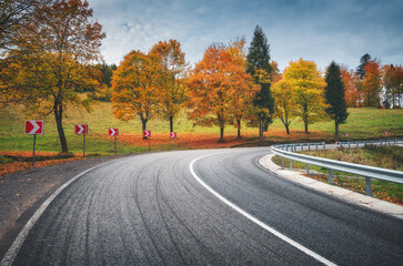 Road in autumn forest. Beautiful empty mountain roadway, trees with orange foliage and overcast sky. Landscape with asphalt road through the woods in fall. Travel in europe. Road trip. Transportation
