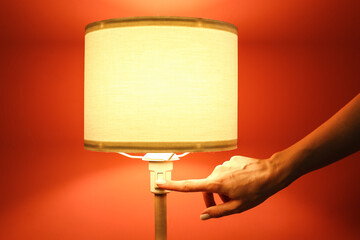 Woman turning off glowing lamp in dark room, closeup