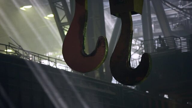 Giant molten metal ladle hooks are moving in the workshop of a metallurgical plant. The rays of the sun shine through the windows of the factory. Ferrous metallurgy. 