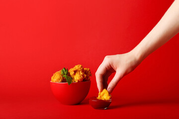 Woman eating tasty popcorn chicken with sauce on color background