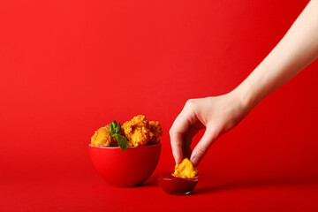 Woman eating tasty popcorn chicken with sauce on color background © Pixel-Shot