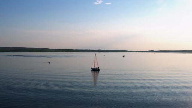 Scenic view of spectacular peaceful wide lake during sunset hour. One sailing yacht swimming on flat water. Natural shot.