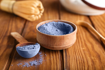 Bowl and spoon with powdered blue matcha tea on wooden background