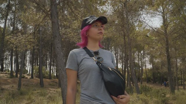 mujer de pelo rosa y con una mochila caminado por el bosque, mujer de camiseta gris y una mochila acerc&aacute;ndose a la c&aacute;mara, mujer deportista dando unos pasos hacia adelante y mirando de frente 