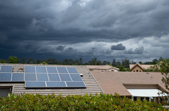 Solar panels appears on the roof of a suburban house with huge storm clouds in the sky.
