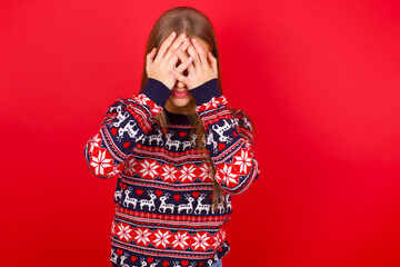 Young caucasian girl wearing christmas sweaters on red background covering her face with her hands, being devastated and crying. Sad concept