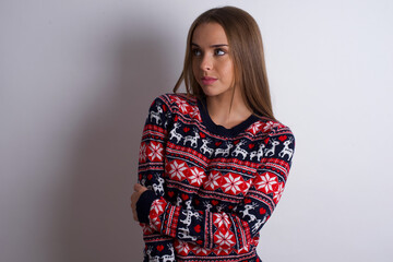 Pleased Young caucasian girl wearing christmas sweaters on white background keeps hands crossed over chest looks happily aside