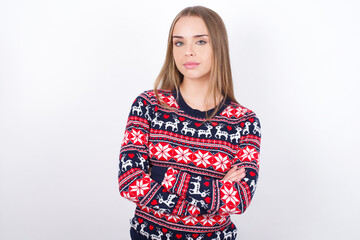 Self confident serious calm Young caucasian girl wearing christmas sweaters on white background stands with arms folded. Shows professional vibe stands in assertive pose.