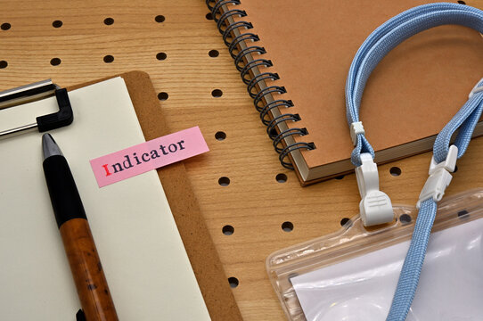 There is a sticky note with the letters Indicator stamped on the edge of a clipboard placed along with a notebook and pen.