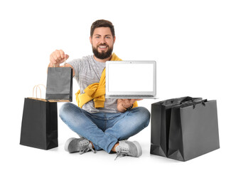 Handsome man with laptop and Black Friday shopping bags on white background