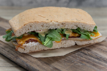 Turkey chedder sandwich on homemade baked bread with bacon served on a wooden platter for breakfast