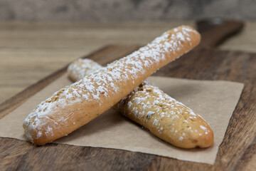 Two lengths of twice baked biscotti sprinkled with powdered sugar and lying crossed on a wooden platter