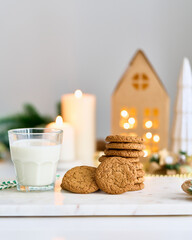 Christmas background with oatmeal and ginger chip cookies, glass of milk. Cozy evening, mug of drink, Christmas decorations with kraft cardboard house home, blurred candles. Selective focus, vertical