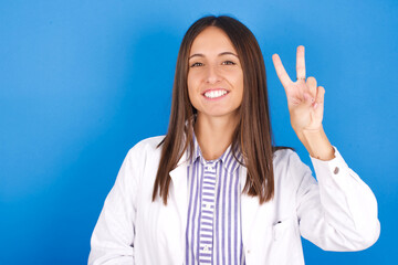 Young european doctor woman on blue background showing and pointing up with fingers number two while smiling confident and happy.