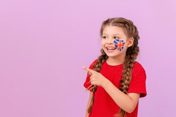 A little girl with an English flag painted on her cheek points to the side and smiles.