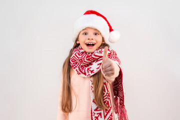 A little girl in a New Year's outfit on an isolated white background points her thumb up and smiles.