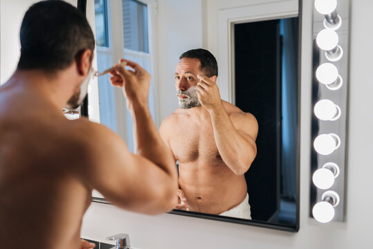Male shaving beard near mirror