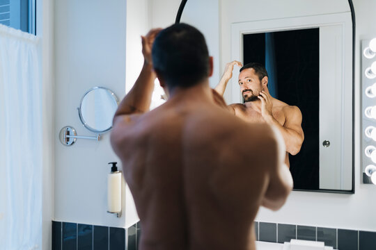 Bearded man looking at bathroom mirror