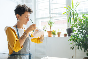 Young woman ceramist applying paint to clay cup