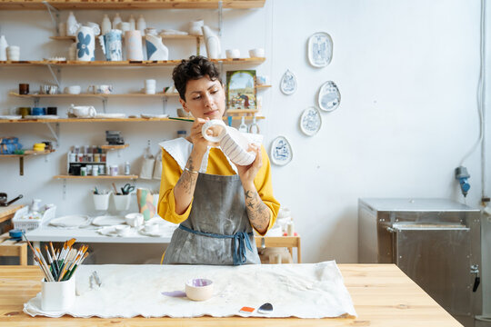 Young woman ceramist applying paint to clay cup