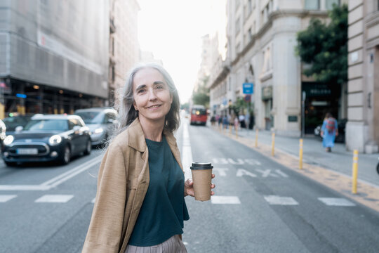 Grey-haired woman with a coffee walking in the street