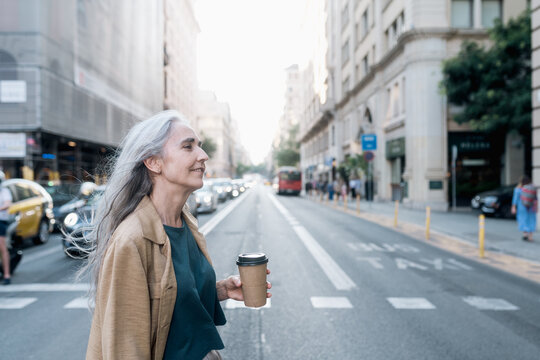 Grey-haired woman with a coffee walking in the street