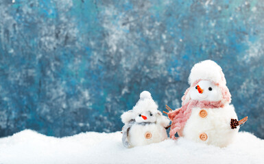 Christmas and new year snow concept with two cute snowmen in hats and scarves in snowdrift on blue background
