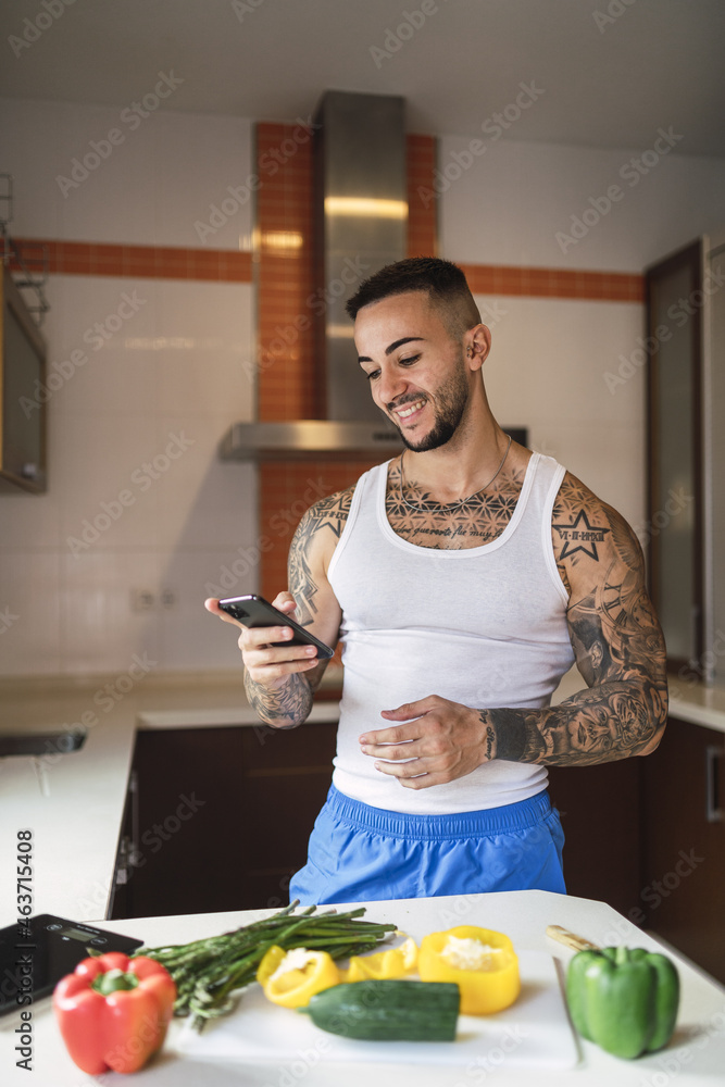 Poster vertical shot of a young tattooed man checking his phone in the kitchen