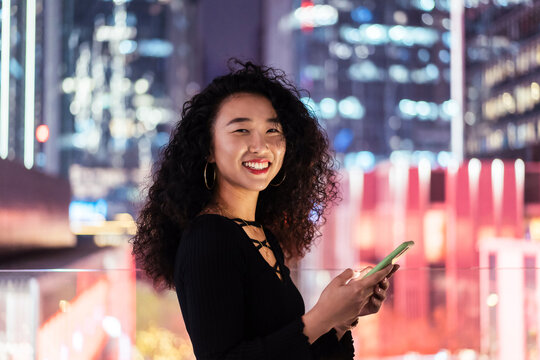 Woman playing phone in front of the night cityscape