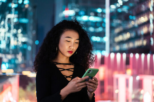 Woman playing phone in front of the night cityscape