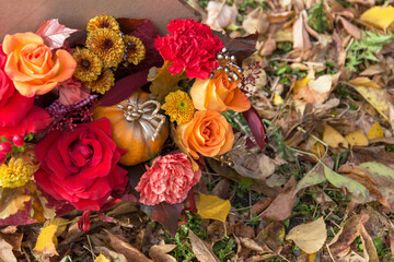 Red orange yellow autumn bouquet with pink rose flowers, fall leaves and pumpkin close up in box by professional florist
