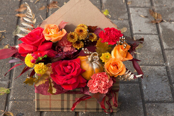 Red orange yellow autumn bouquet with pink rose flowers, fall leaves and pumpkin close up in box, envelope, gift