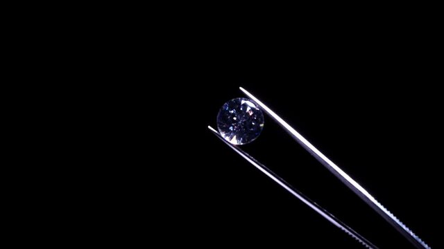 Close up of diamond held in tweezers, selective focus. View under magnifying glass. Round cut luxury brilliant stone jewellery. Engagement and marriage or wedding purchase. Quality Inspection.