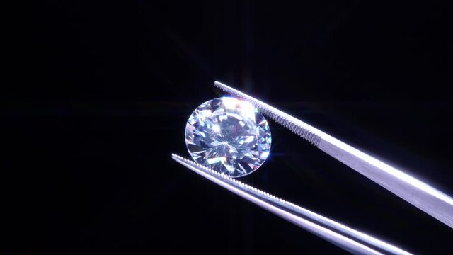 Hand held in tweezers diamond quality Inspection, selective focus. Chips and damage look up. Macro close up of luxury brilliant. View under magnifying glass. Round cut stone jewellery. Engagement day