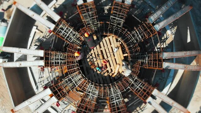 Aerial view of cooperative industrial workers wearing hardhats and safety vests working on round building in sunny weather. Building production. Construction site.