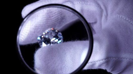 Goldsmith hands in white gloves inspect the quality of luxury brilliant diamond. Selective focus, macro. Precious stone shine in the light with star rays. Round diamond for Engagement or wedding ring - Powered by Adobe
