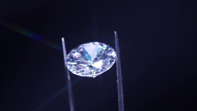 Close up of diamond held in tweezers, selective focus. View under magnifying glass. Round cut luxury brilliant stone jewellery. Engagement and marriage or wedding purchase. Quality Inspection.