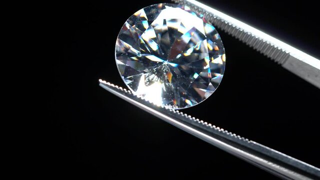 Diamond stone hold in tweezers. Brilliant cut or crystal rock in metal jeweller tongs. Craft jewelery making or hobby in studio. Macro shot of inspection and manufacturing of luxury jewellery.