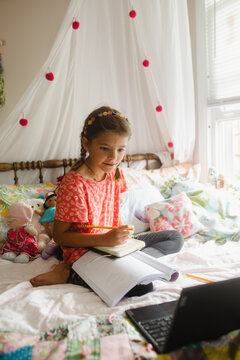 Girl attending homeschooling class through laptop in her bedroom