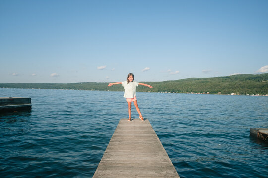 Girl does yoga poses on dock of lake