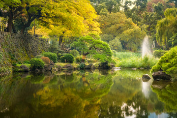 Beautiful and peaceful nature corner with a fountain and reflectons in the pond's water in autumn at Hibiya Park in Chiyoda City, Tokyo, Japan.