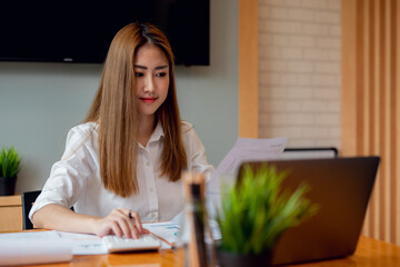 Professional young business Asian woman using computer laptop and Talking On Phone On In Modern Home Office. a calculator to calculate the numbers, report finance accounting concept.	