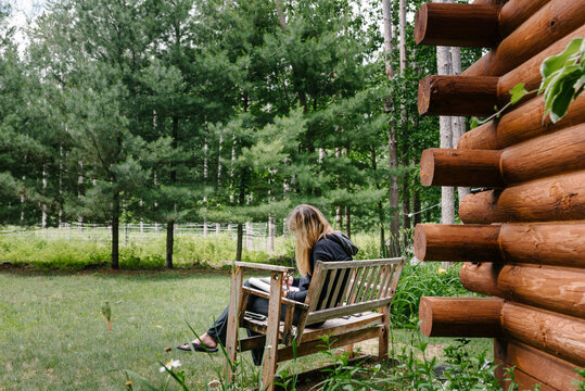 Anonymous woman drawing on a bench by a log cabin