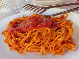Spaghetti and sauce on white plate with metal serving tongs
