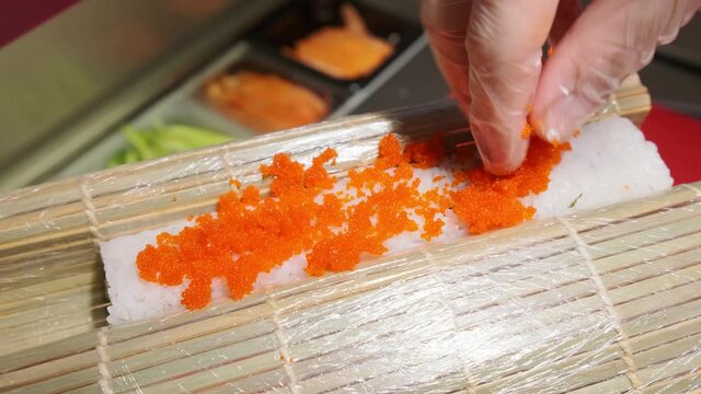 The sushi chef sprinkles tabiko caviar on the rice roll on the mat. Asian cuisine, Sushi restaurant. Cooking rolls. Shot in 4k.
