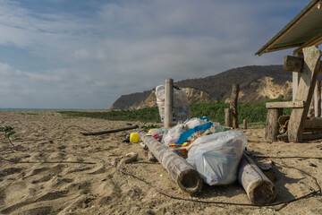 A pile of trash on the beach next to a mountain on a sunny day.