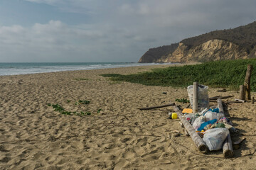 A pile of trash on the beach next to a mountain on a sunny day.