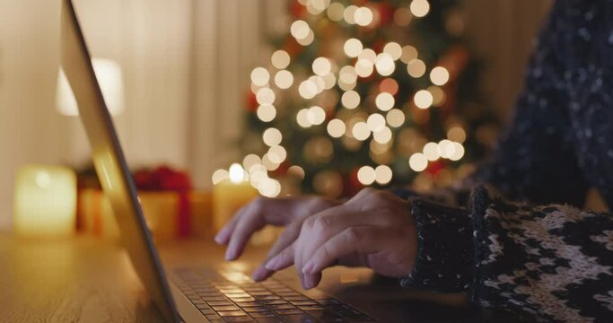 Close-up hand enter search gift card on web page sending Merry Xmas eve wishing text or chat on e-mail working on laptop at home. Good warm time cozy Night winter season with tree light inside house.